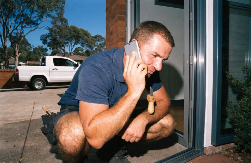Australian tradesperson on a phone call while crouched at the entry of a house