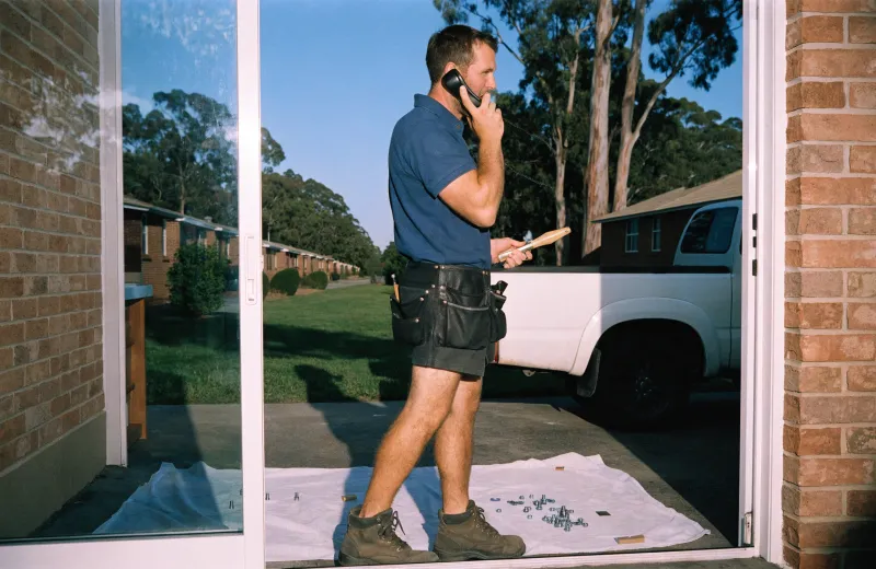 Australian tradesperson with a tool belt standing in a doorway taking a phone call