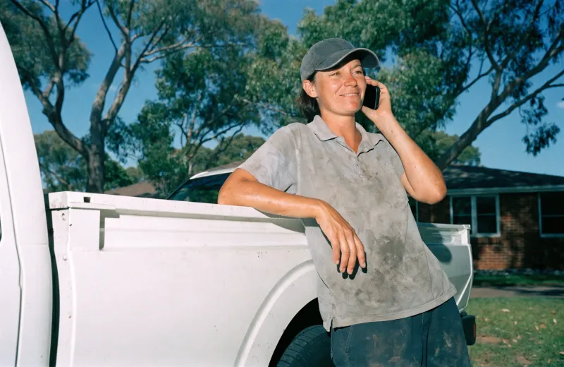 Australian tradesperson leaning against a ute answering a phone call on site