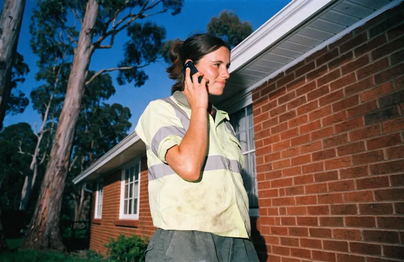 Australian tradesperson in a hi-vis shirt on a phone call outside a brick house
