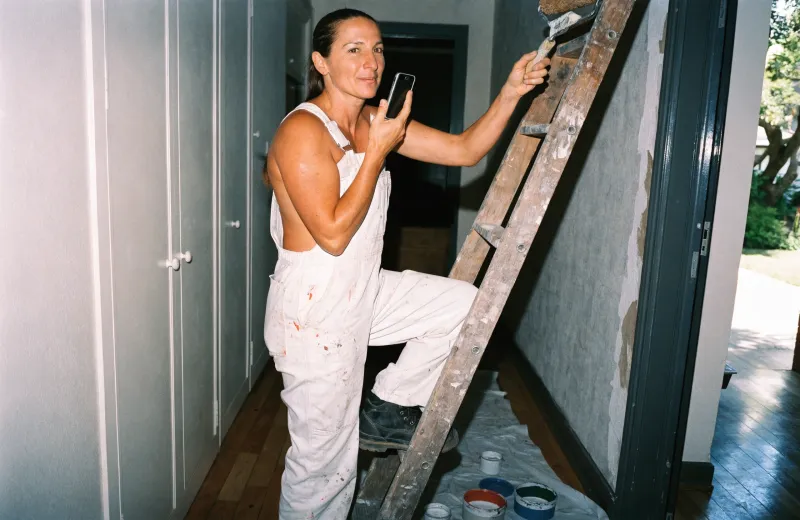 Australian painter on a ladder holding a phone while painting a wall